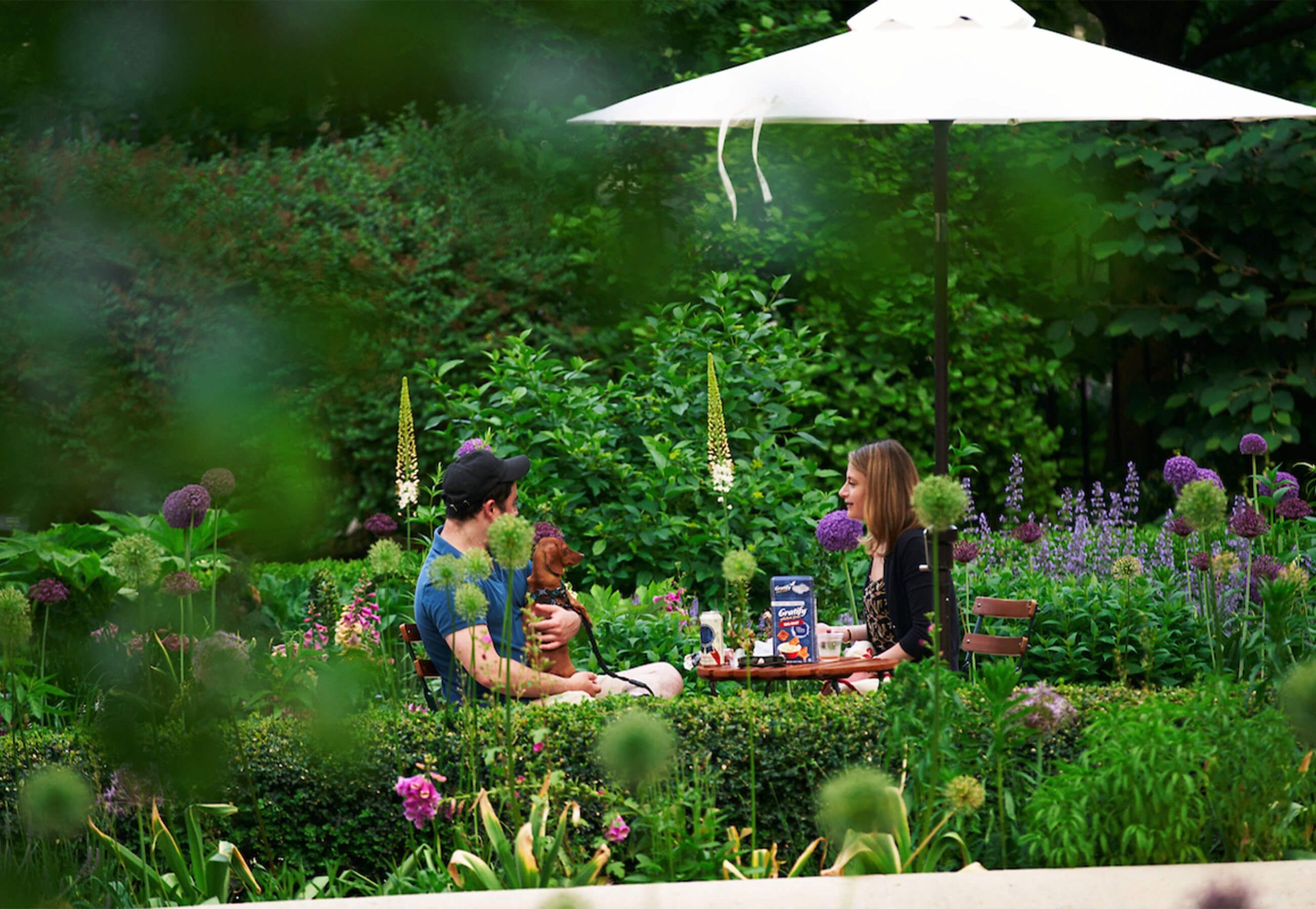 The Rodin Museum Garden Bar Returns May 29 With a New Food Truck and a Crossing Choir Performance 5 A couple at a bistro table with their leashed dachshund at the Rodin Museum Garden Bar, surrounded by alliums and foxglove in bloom.