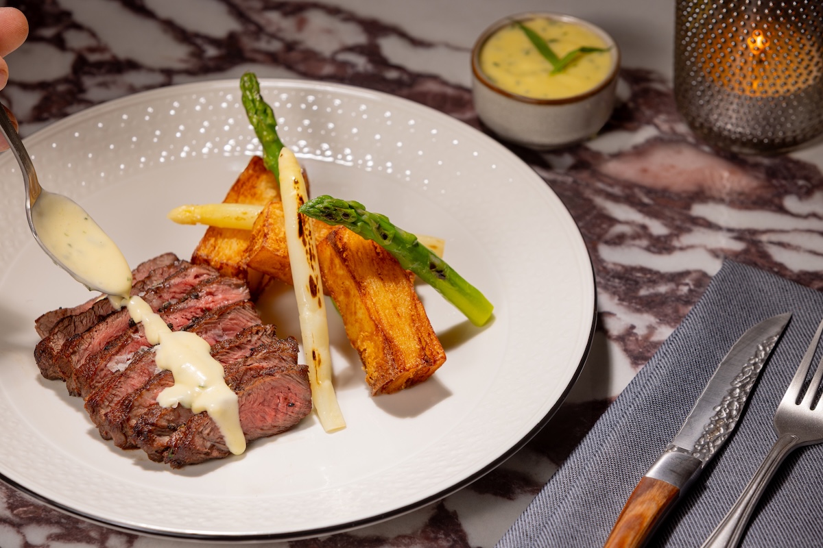 Steak entrée being finished with sauce alongside roasted vegetables at Merrick's Tavern