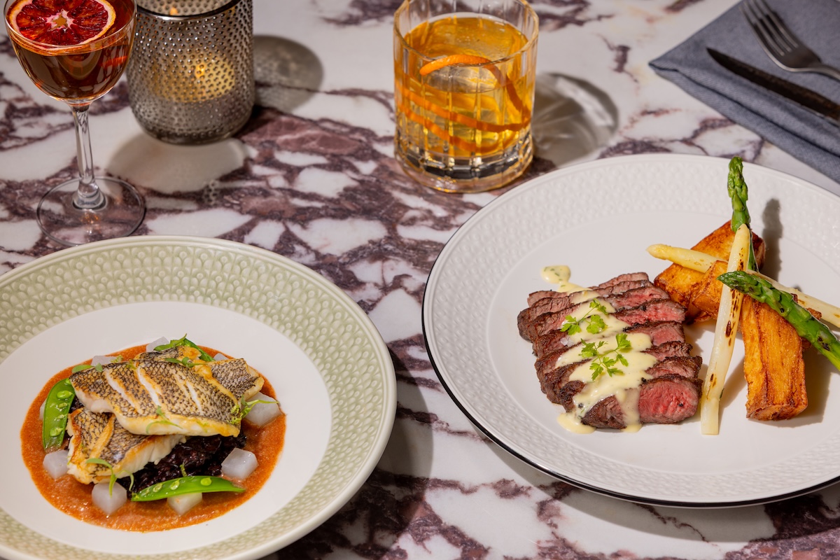 Plated steak and fish entrées with cocktail and candle on the marble tabletop at Merrick's Tavern